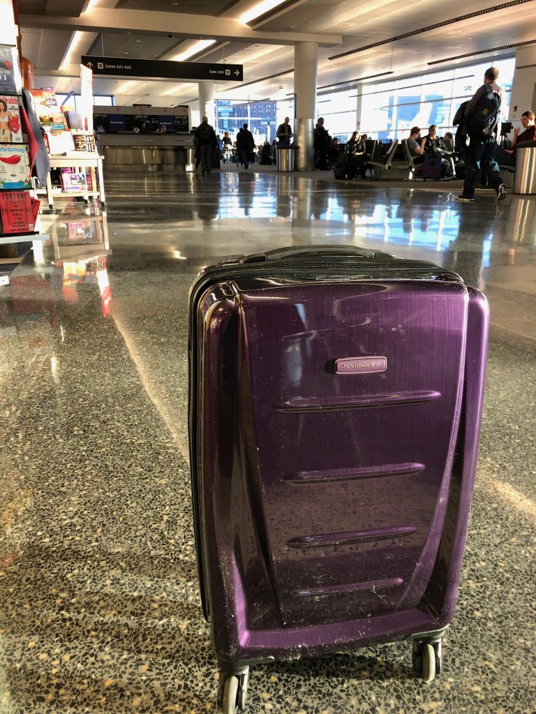 A purple suitcase standing upright in a busy airport