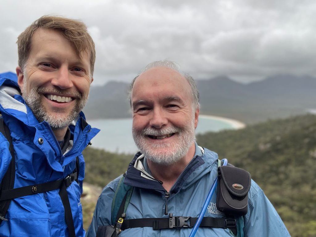 Ken and an older man, smiling in the rain atop a cliff