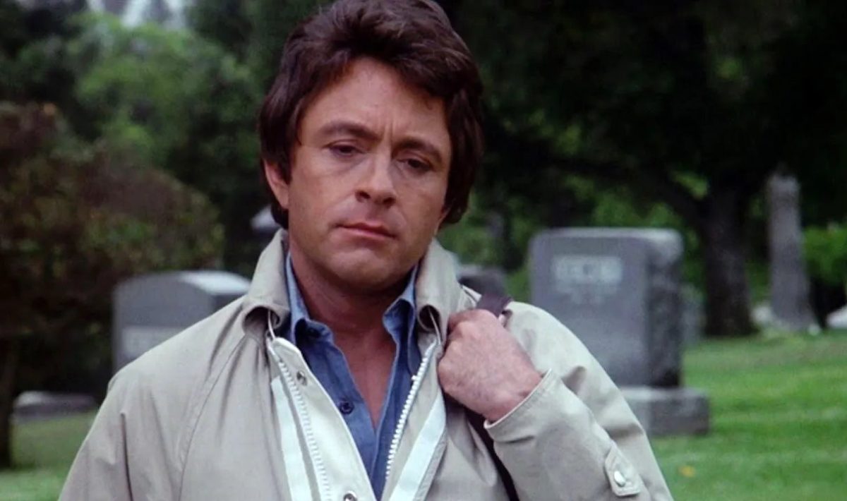 Bill Bixby, a bag slung over his shoulder, walks away from a cemetery