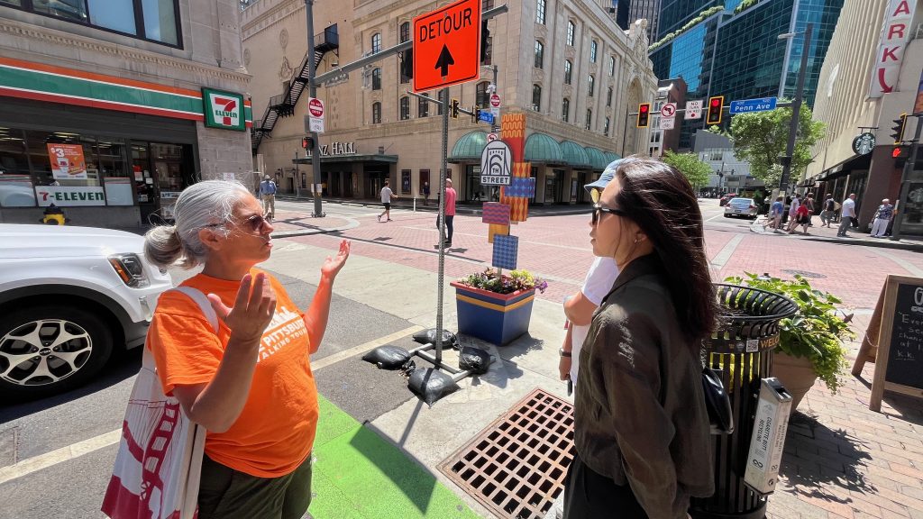A woman in a orange shirt guiding a tour group through downtown Pittsburgh