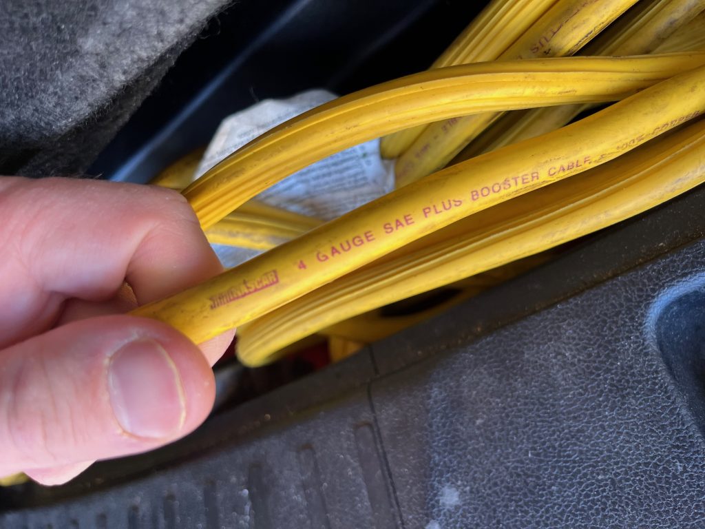 A hand holding yellow, 4-gauge jumper cables