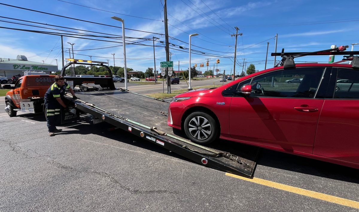 A red Prius being hauled up onto a tow truck's flat bed