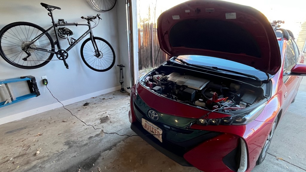 A Toyota Prius Prime with cables running from under the hood to a nearby A/C outlet