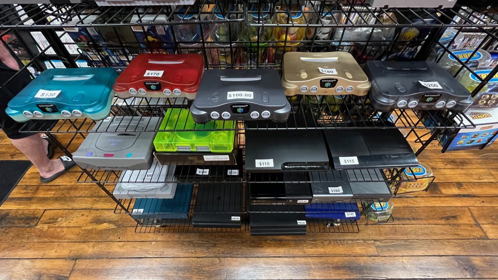 Shelves of used video game consoles with price stickers